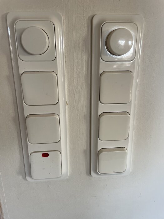 Vägg med två vita dimmerpaneler av märket TREND, en med en röd indikatorlampa och liknande rattar för ljusreglering.