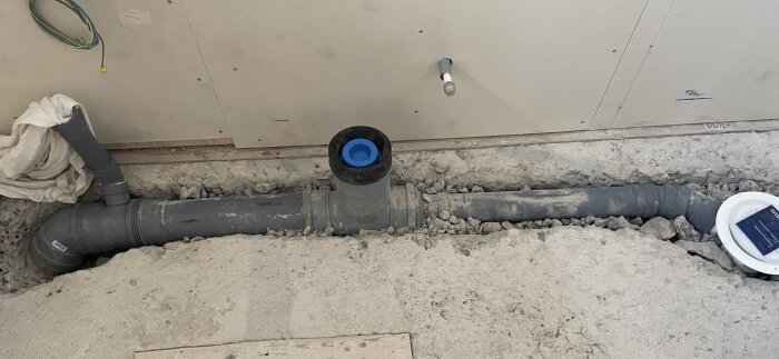 Gråa avloppsrör i ett öppet golv med bland annat ett T-rör och en 45-gradersböj synliga mot en vägg. Ställer frågor om korrekt installation.