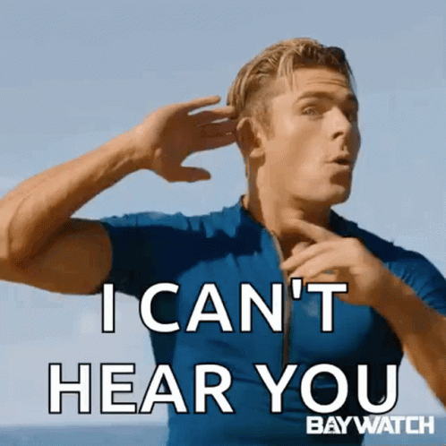 En man i blå tröja placerar handen vid örat med texten "I CAN'T HEAR YOU", mot en strandbakgrund. Från filmen Baywatch.
