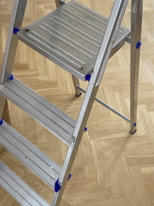 Aluminiumstege med tre steg och en plattform placerad på träparkettgolv.