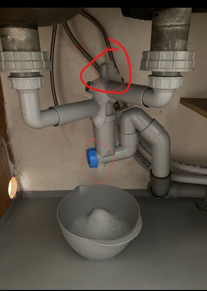 Vattenlås under diskbänk med rör och avstängningsventil; skål med diskmedelsskum syns under. Röda markeringar visar rördetaljer.