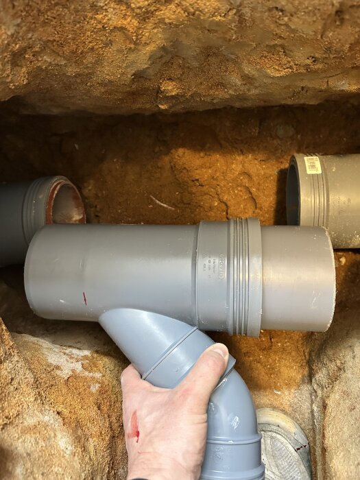 Hand som håller ett nyligen installerat grenrör av plast i en jordgrop.