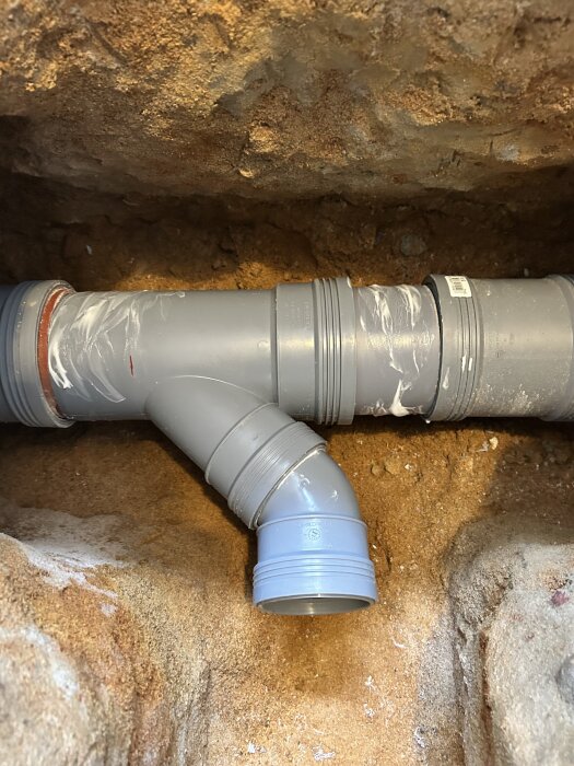 Grått grenrör installerat i en grävd sandgrop med skjutmuffar synliga, redo för att fyllas igen med sand.