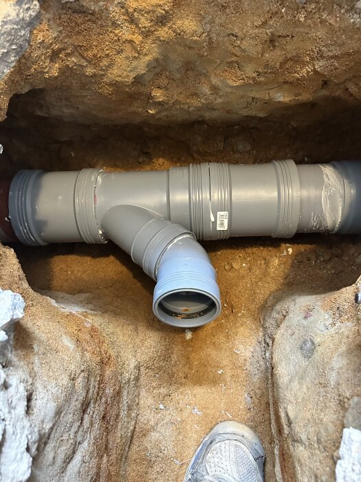 Plastgrenrör installerat i en grävd grop med sand runtomkring, klart för återfyllning.