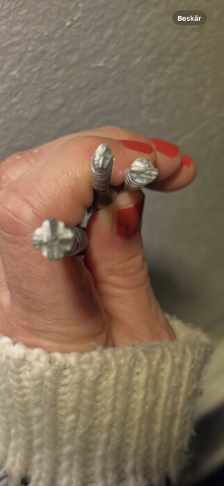 Hand som håller tre skruvar med olika skalle, alla av metall.