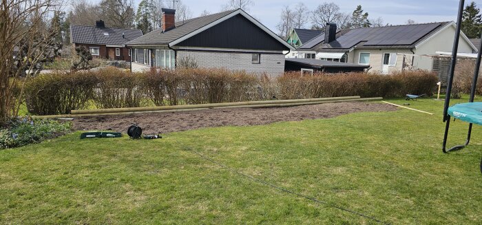 En trädgård under arbete med nyplanterad gräsmatta, byggtimmer längs kanten och verktygslådor på gräset.