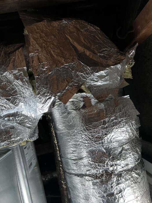 Isolering med aluminiumfolie som lossnat från ett ventilationsrör på en kallvind.
