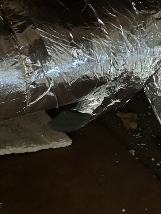 Ventilationsrör på kallvind med lossnande isolering av stenull, täckt med reflekterande tejp.