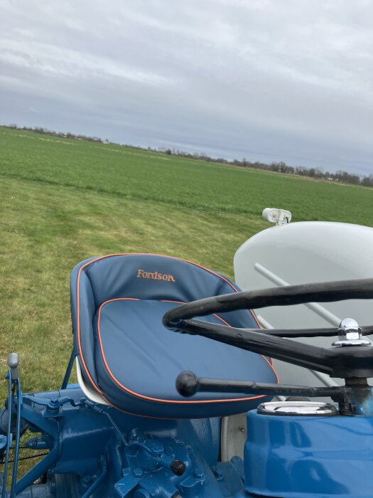 Klassisk blå Fordson-traktor stående på en grön åker, med fokus på sätet och ratten.
