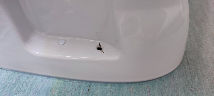 Sprucken del av toalettstol vid skruvhål, skada försökt lagas med lim, synliga sprickor runt hålet.