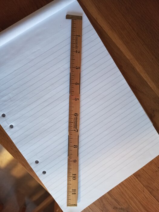 Tumstock med millimeterindelning ligger på ett linjerat papper på ett träbord.