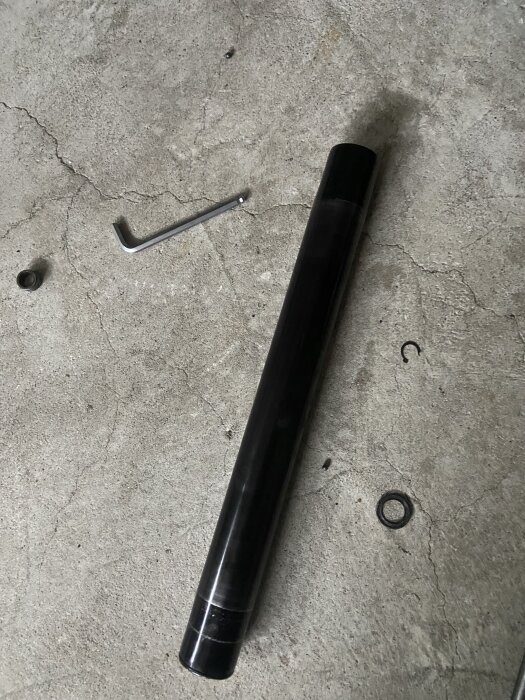 Metallcylinder på golvet med en insexnyckel och små delar bredvid.