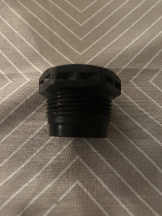 Svart plastplugg med gängor på randigt tyg.