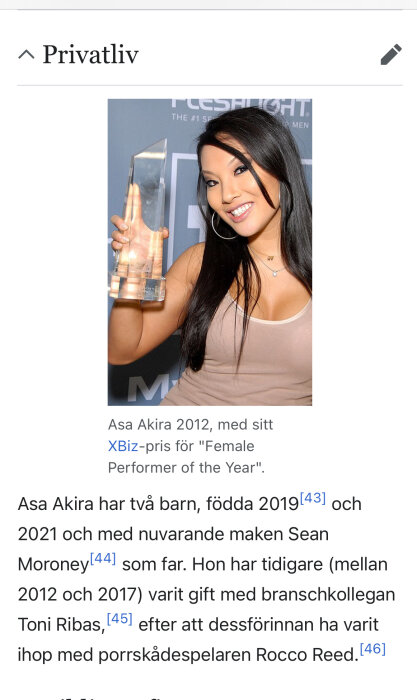 En person håller ett pris och ler framför en bakgrund med text.