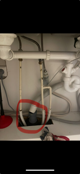 Avloppsrör under diskbänk med snett ställd nederdel markerad i röd cirkel; röranslutningar och slangar synliga.