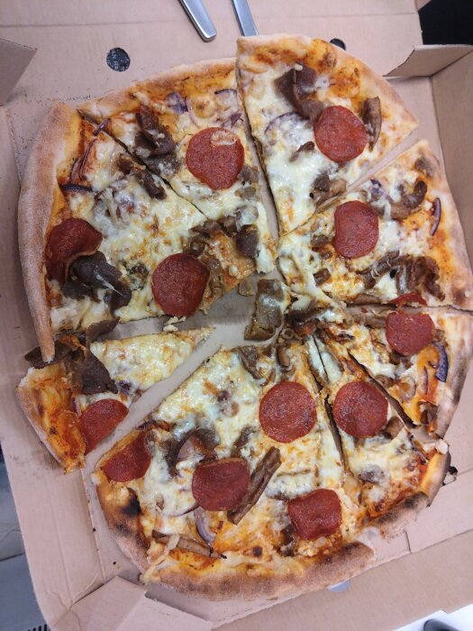 Pizza med pepperoni och kött, ojämnt skuren i en kartong.