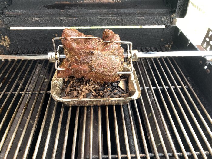 Lammstek på grillspett i gasolgrill, ovanpå en foliform med rökspån.
