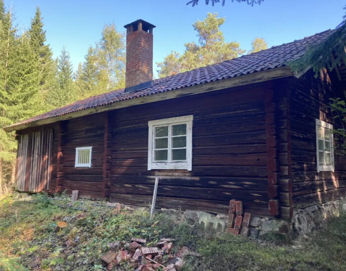 Gammal fäbod i trä med tegelpannor och en skorsten, belägen i skogsmiljö i Dalarna. Bakgrund med träd och skogsdunge.