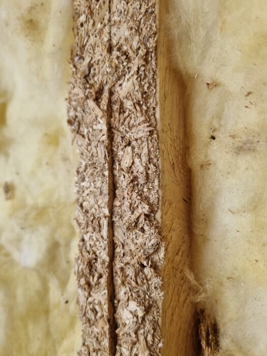 Rester av spånskiva fast i träregel bredvid isolering.