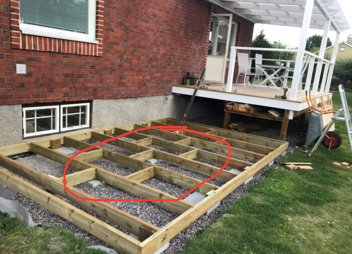 Träram byggs för altan, med reglar mellan skruvreglar markerade i rött, inga balkskor används, intill husvägg av tegel.