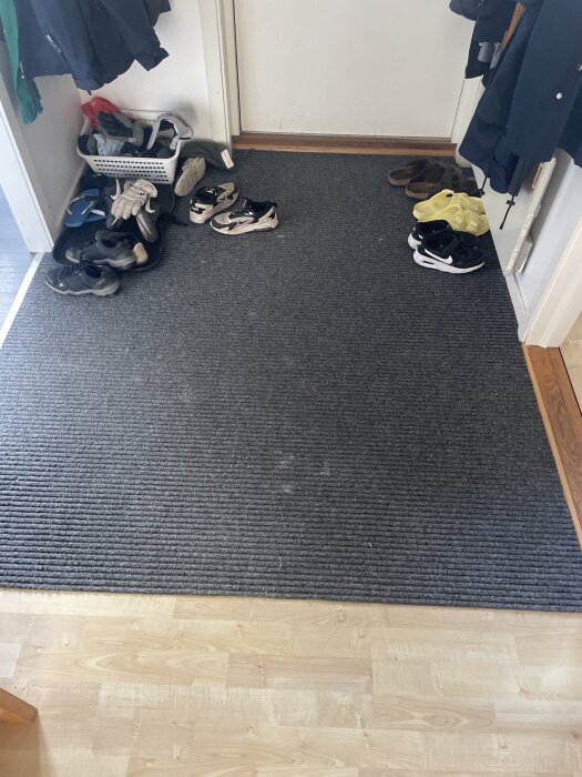 Grå heltäckande entrématta med gummibaksida i hall, flera par skor placerade runt om.