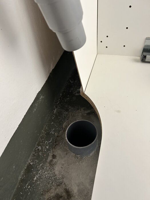 Grått avklippt avloppsrör i hörnet av ett rum, fel installerat för vaskanslutning.