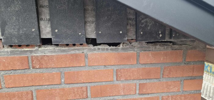 Mörka trälister monterade ovanpå tegelvägg, synliga hål mellan tegel och panel.