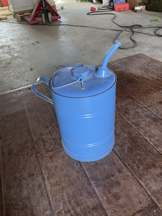 Blå metallbehållare med pip och handtag på ett betonggolv i garage. Möjligen en gammal fotogendunk.