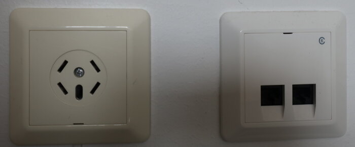 Ett gulnat eluttag bredvid ett nästan oförändrat nätverksuttag på en vägg i ett äldre installationsprojekt från Elko RS-serien.