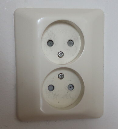 Gulnat eluttag från Elko RS serien med två uttag och synliga skruvar, monterat på en vit vägg, visar solblekning över tid.