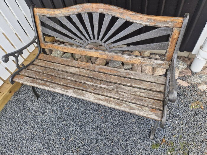 Gammal trädgårdsbänk med flagnande lack och metallstöd, står på en grusgång.