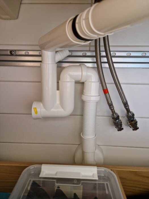 Under-bänken avloppsinstallation med rör och vattenlås anslutet till två flexibla slangar mot väggen.