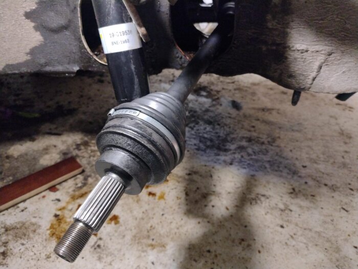 Högra drivaxeln på en Saab, nyligen renoverad, sitter monterad i bilens hjulhus på ett cementgolv i ett garage.