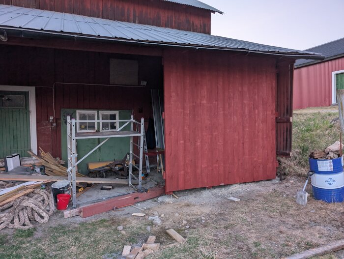Röd panel monterad på traktorgarage, omgiven av byggmaterial och ställning.