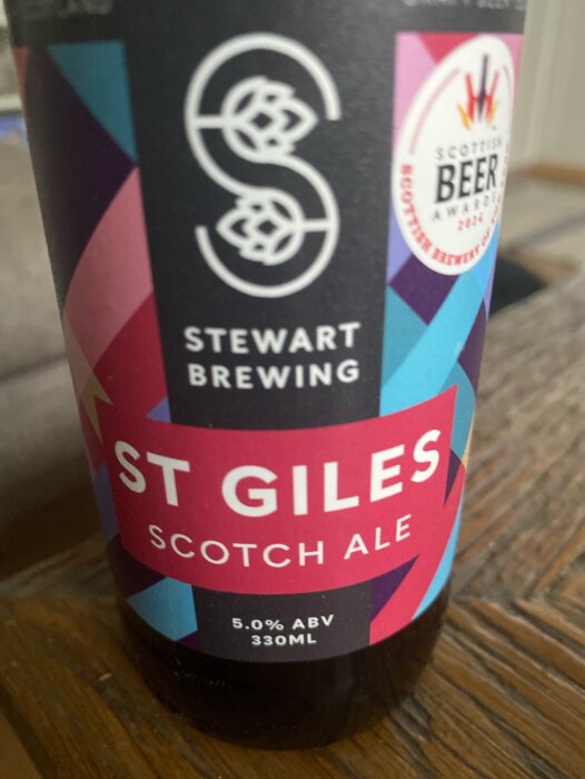 Flaska av St Giles Scotch Ale från Stewart Brewing, etikett med färgglada geometriska mönster och text om alkoholhalt.