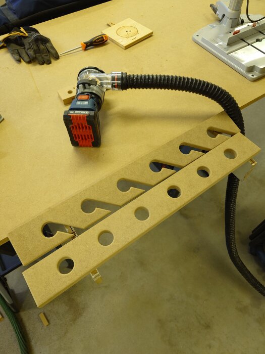 Spöhållare under konstruktion i trä med hål och urtag, omgiven av verktyg på arbetsbänk i ett garage.