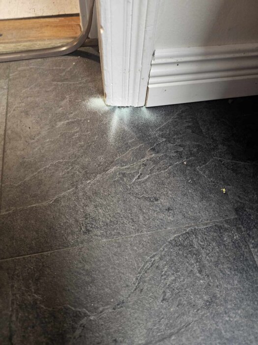 Glittrigt pulver bredvid golvlist på mörkt golv efter användning av IKEA Nivå underlagsgolv.