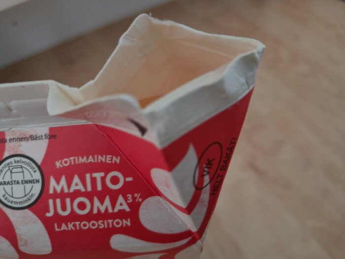 En öppnad mjölkförpackning med finsk text på en mjölkfri dryck, 3% fett, röd och vit design, står på ett ljust golv.
