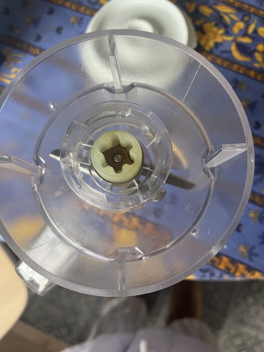 Mixerdel med plastkåpa sedd uppifrån, monterad över bord med mönstrad blå duk.