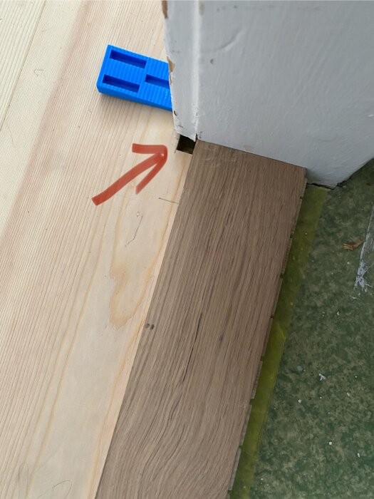 Laminatgolv med glipa vid dörrkarm, blå distanskloss och röd pil markerar problemet.