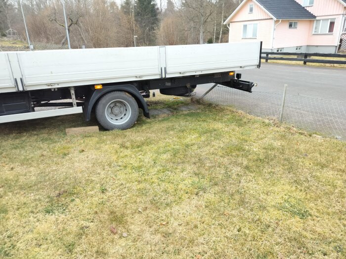 Lastbil sitter fast i trasigt nätstaket på gräsmatta nära en väg, vid ett hus med tiden halvklart väder.