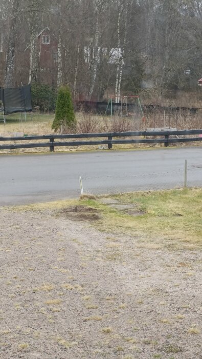 Ett trasigt staket vid en väg, omgiven av gräsmatta och träd.