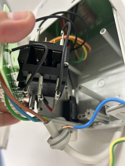Hand håller i en elektrisk komponent med flera anslutna kablar i olika färger i ett reglage.