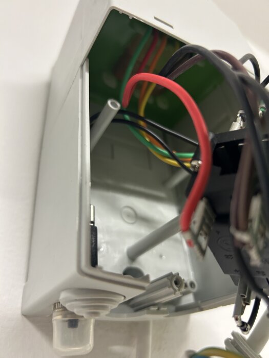 En vit regulatorbox med flera exponerade kablar i olika färger, inklusive röd, gul och svart, syns i närbild.