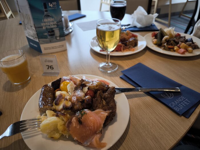 Tallrik med buffémat inklusive lax, potatis och ägg på ett bord med drycker och Grande Buffet-servetter.