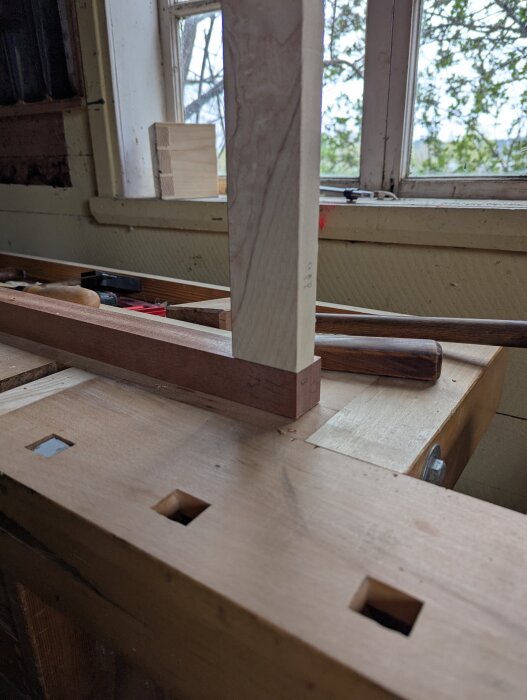 Träbearbetningsprojekt i ett rustikt skjul, där tapphål syns i arbetsbänken med ett fönster i bakgrunden.