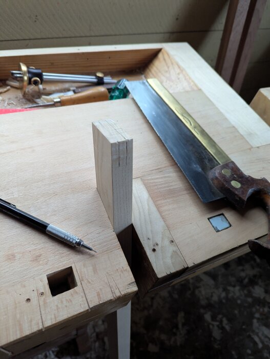 Arbetsbänk med träarbete, verktyg som såg, skruvmejsel och blyertspenna, samt påbörjat tapphål.