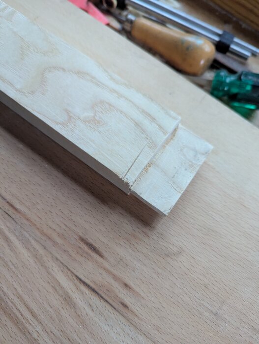 Träbit med urfrästa tapphål på en arbetsbänk, omgivna av verktyg, en del av ett byggprojekt.