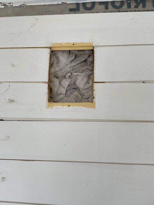 Utskuren del av vit väggpanel visar en nisch med en handduk instoppad, använd som tätning i spjäll.