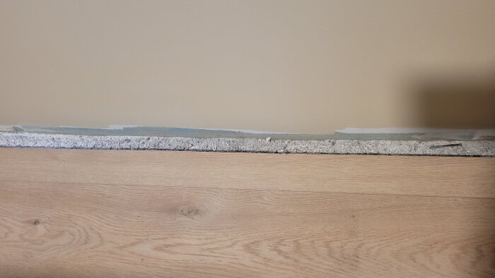 Närbild av en vägg med en synlig springa vid golvet där listen har avlägsnats, visar underlaget som behöver täckas.